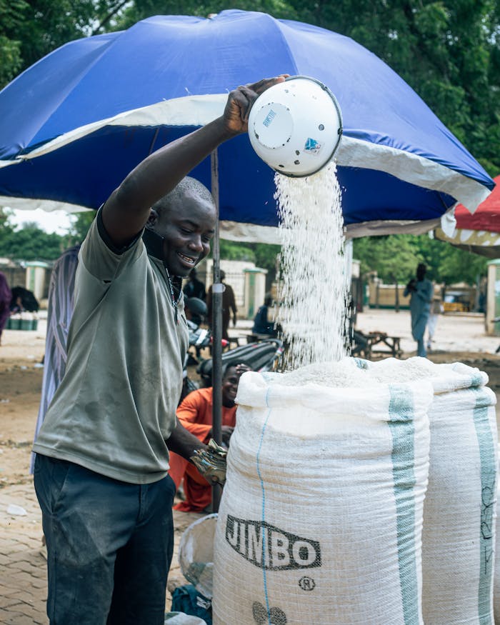 A man pours grains into a large sack at an outdoor market, showcasing local trade.